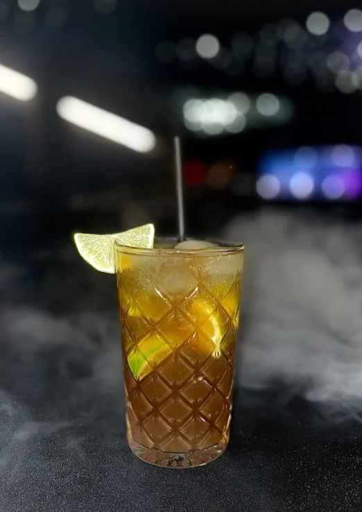 Cuba Libre ambré dans un verre à facettes, avec du citron vert